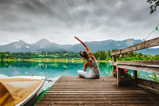 Reconnection to Nature – Outdoor Meditation and Yoga during sunrise on a jetty at Lake Faak, Austria, looking at mountain Mittagskogel/Kepa, the third highest mountain of the Karawanks mountain range