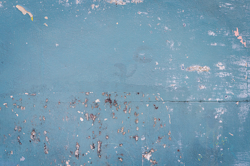 Part of an old blue concrete wall with cracked and peeling paint.