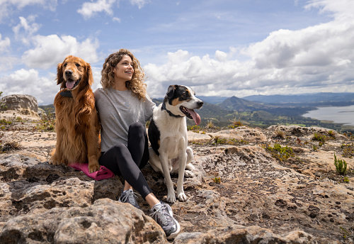 Portrait of a young Latin American woman hiking with her dogs in the mountains and taking a break