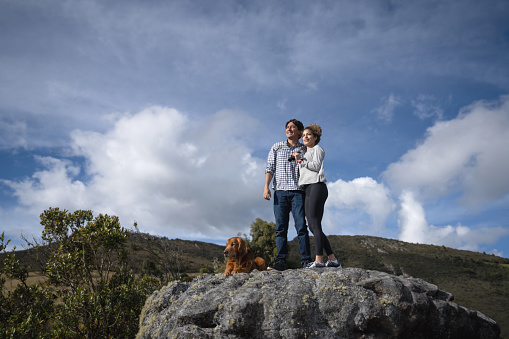 Loving Latin American couple looking happy at the top of a mountain while hiking together with their dog