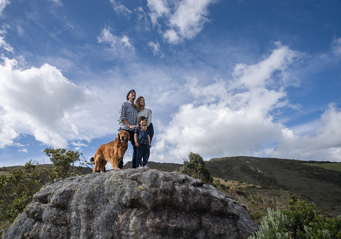 Happy Latin American family smiling on the top of a mountain while having fun hiking with their dogs