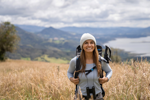 Portrait of a happy woman hiking in the mountains and smiling while carrying her backpack - lifestyle concepts