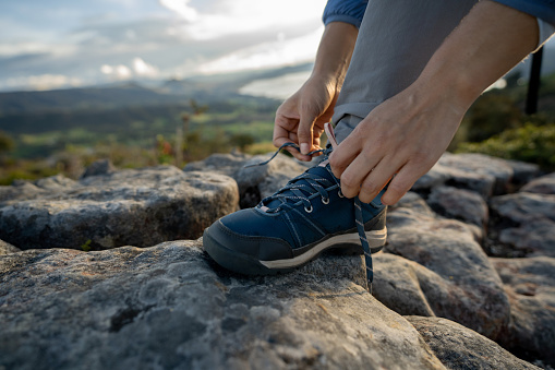 Close-up on a woman tying the shoelaces of her hiking boots while hiking in the mountains - outdoor lifestyle concepts