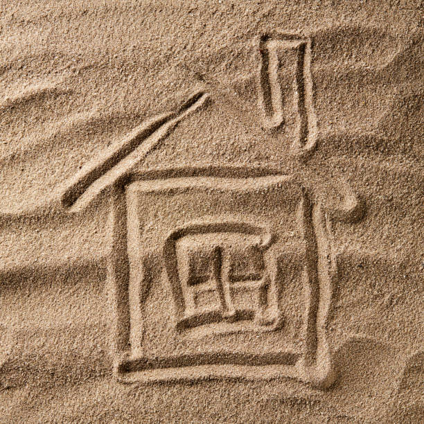 istock house symbol drawing on beach sand. hard shadow. property concept 1286612911