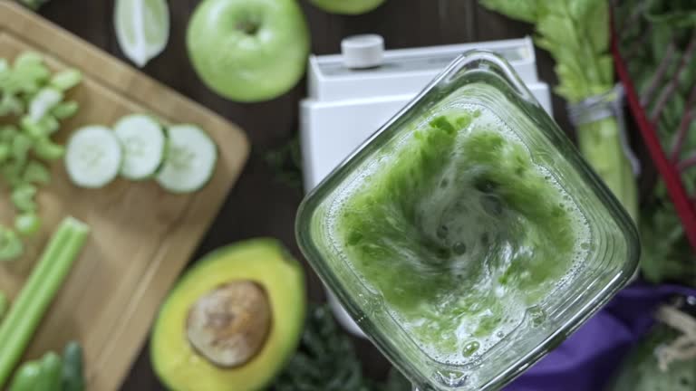 Diets concept: Slow motion of directly below shot of blender mixing vegetables and fruits for detox smoothie. Cutting board and blender mixing on kitchen table