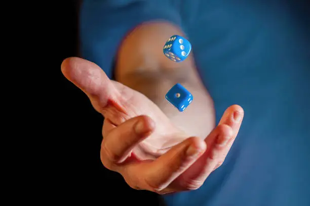 Photo of Caucasian male hand throwing blue dice cubes in the air - closeup with shallow focus