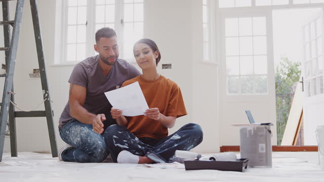 Couple sitting on floor wearing old clothes with paint chart ready to decorate new home - shot in slow motion