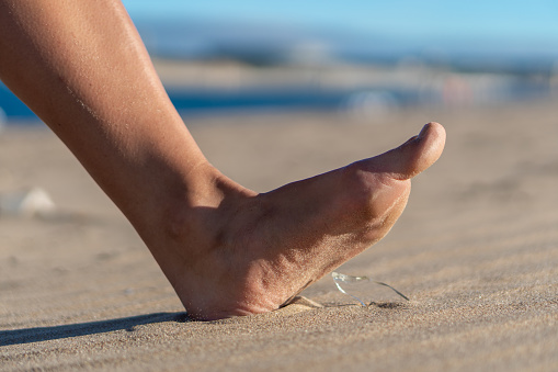 Woman going on the beach and risking of stepping on a splinter of broken bottle glass, which is lying on the littered sand