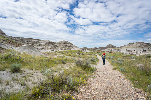 Cute Redhead Boy Hiking in Badlands of Dinosaur Provincial Park in Alberta, Canada. It is a beautiful summer sunny day. He is wearing a backpack and hiking in the park’s footpath.
