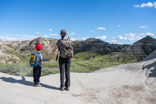Mother and Son Hiking in Badlands of Dinosaur Provincial Park in Alberta, Canada. It is a beautiful summer sunny day. They are holding hands and bonding while hiking in the park’s footpath.