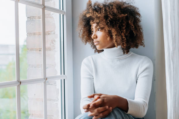istock Thoughtful young woman sitting on modern white windowsill 1286619178