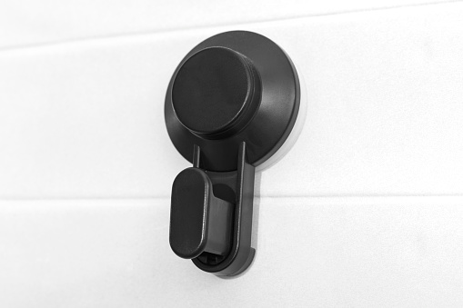 Black plastic hook for hanging clothes, towels on a background of white glossy tiles. Plastic wall hanger, close up