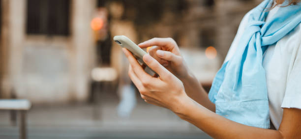 Close-up photo of female hands with smartphone. Young woman typing on a mobile phone on a street Close-up photo of female hands with smartphone. Young woman typing on a mobile phone on a sunny street person on phone stock pictures, royalty-free photos & images