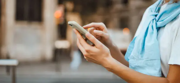 Photo of Close-up photo of female hands with smartphone. Young woman typing on a mobile phone on a street