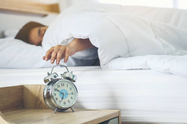 istock Alarm clock that set the time to wake up with the sleeping man refusing to wake up as the background is blurred. 1286626171