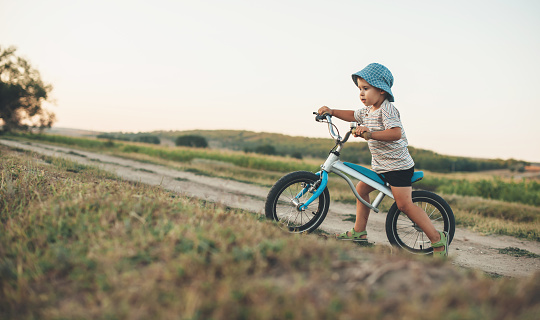 Side view photo of a caucasian boy with blue hat riding a bike on a country road