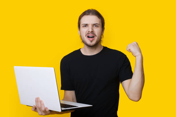 istock Bearded caucasian man is gesturing the yes sign on a yellow studio wall while holding a laptop 1286628527
