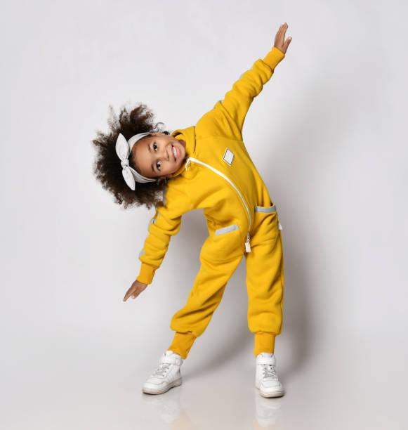 Frolic dark-skinned a kid girl in yellow sport jumpsuit performs sideways bands, warmup, morning gymnastics stock photo