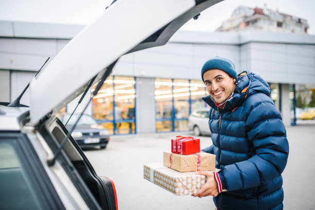 istock Smiling young man holding presents loading his car trunk. Consumerism / shopping concept. Special occasion / holiday shopping concept. 1286640141