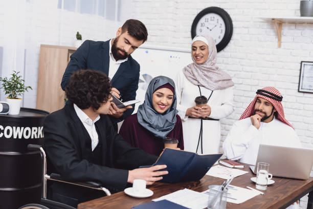 istock Disabled arab man in wheelchair working in office. Man is sharing notes with coworkers. 1286642652