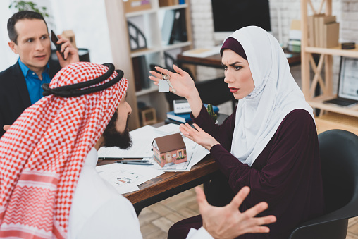 Muslim couple is quarreling in office of real estate agency. Real estate buying concept. Arabic man in kufiya is arguing with Arab woman in hijab in office of Real Estate Agent.