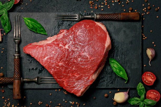Raw beef steak on a stone cutting board and forks. Grass-fed meat with spices and herbs. Food flat lay Raw beef steak on a stone cutting board and forks. Grass-fed meat with spices and herbs. Food flat lay grass fed stock pictures, royalty-free photos & images