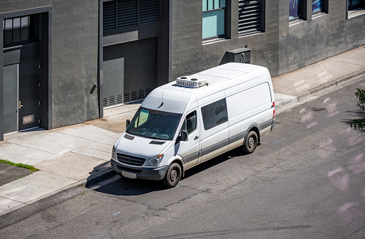 Compact commercial cargo mini van for delivery and small business services standing on the urban city street with multilevel apartments buildings