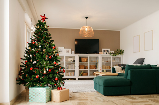 Decorated Christmas tree with gifts underneath. Wide angle photo with whole cosy living room visible. Christmas morning. No people. Daylight.