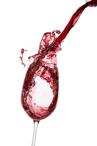This is a photograph of a glass of red wine spilling over as it is being poured into from a bottle on a white background