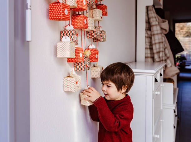 piccolo bambino curioso che apre il primo regalo del calendario dell'avvento fatto a mano appeso a parete. natale sostenibile. festeggiare a casa, infanzia curiosa. - advent calendar advent christmas childhood foto e immagini stock