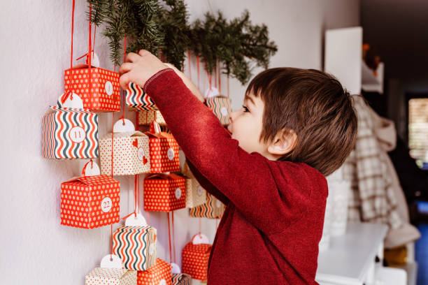 pequeño niño curioso feliz abriendo el primer regalo del calendario de adviento hecho a mano colgando en la pared. navidad sostenible. celebrando en casa, en la infancia. - advent calendar advent christmas childhood fotografías e imágenes de stock