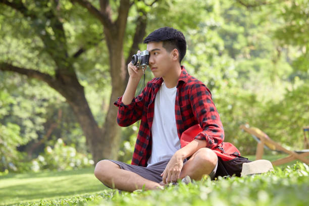 istock Happy Asian man backpacker sitting on the grass field on a summer day 1286652949