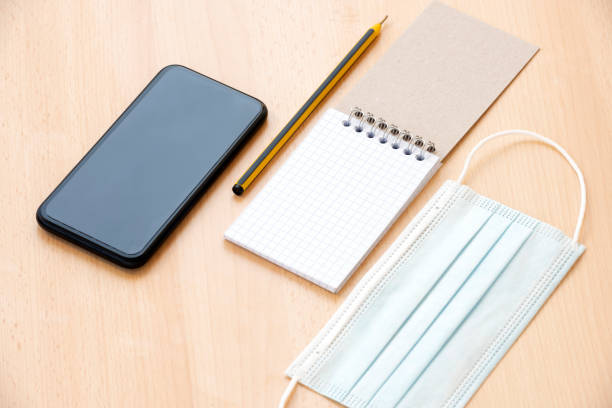 istock A face mask, a blank spiral notepad with a pen and a smartphone are arranged on a wooden table. To-do list concept during the Covid-19 Outbreak. 1286653357