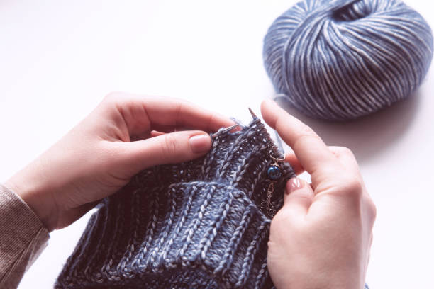 istock Female hands with knitting needles to knit wool sweater on white background 1286656461