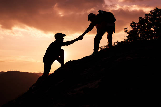 istock Silhouette of hiker helping each other hike up a mountain at sunset. 1286659266
