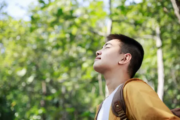 Asian teenager breathing deeply fresh air in a forest.