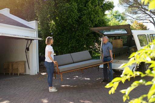 Caring Dad helping excited daughter move into her new apartment.  They are carrying a sofa couch from a truck outdoors.