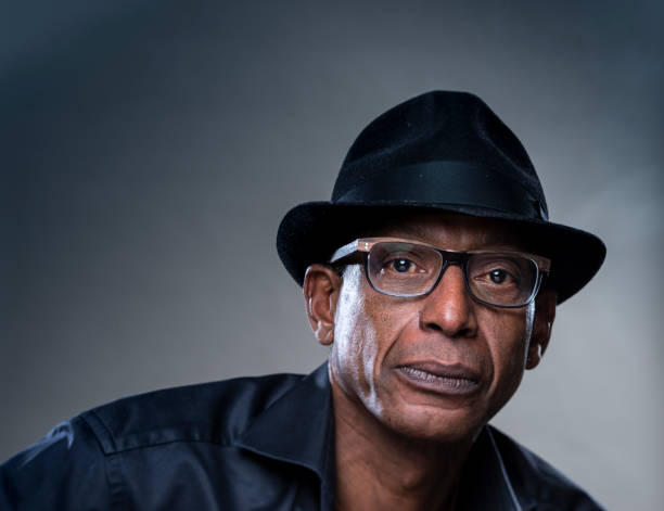 istock Real Man with a serious Expression. Portrait of a real man with black hat on a gray background. 1286663813