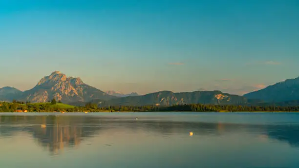 Germany, Allgaeu, Hopfensee lake water reflecting mountains and forest nature landscape in warm sunset light in summer