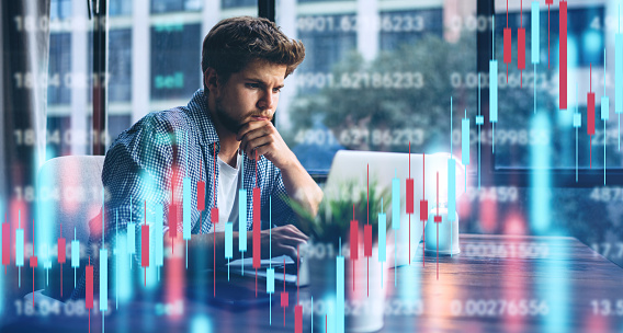 Young man working at modern office.Technical price graph and indicator, red and green candlestick chart and stock trading computer screen background. Double exposure. Trader analyzing data