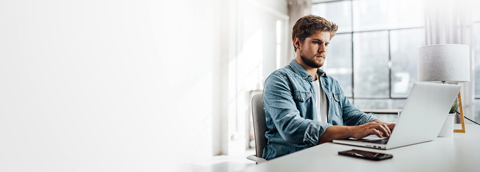 Young man typing on laptop. Modern businessman at sunny office. Freelancer at work. Blogger or journalist writing new article. Copy space for text