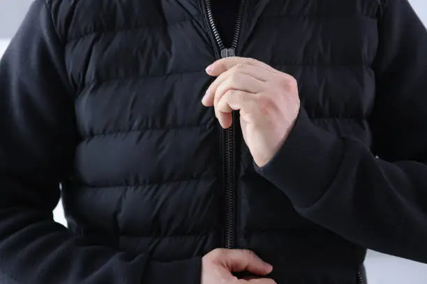 Photo of Man zips up a black jacket closeup