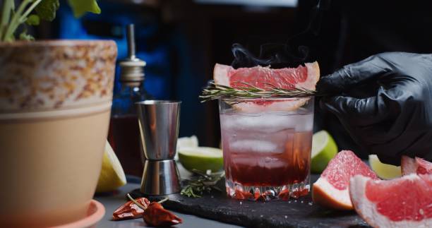 Human hands are making a mocktail with various citrus juices and smoking rosemary