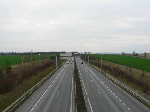 istock Empty highway on a cloudy day. A speeding car. View over the two-way road with two lanes in each direction. Green field along the road, autobahn or highway. 1286672058