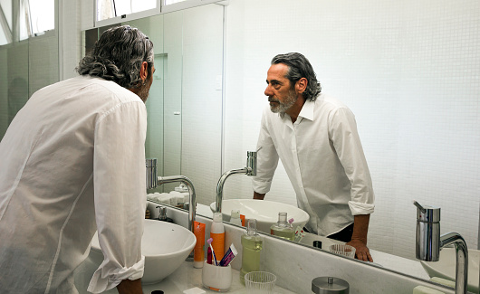 Handsome mature man looking at himself at the mirror in a bathroom
