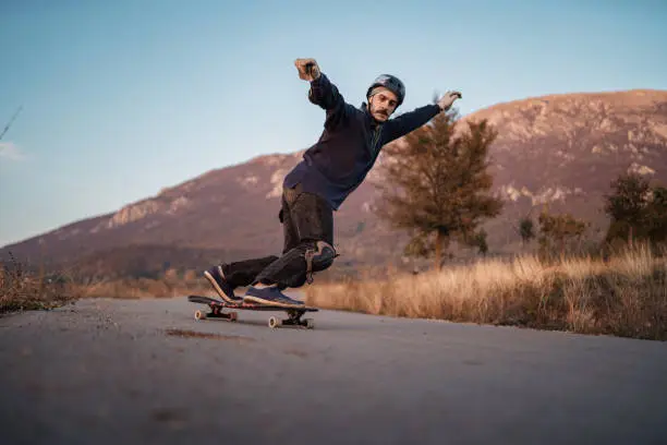 Photo of Extreme sports lover riding longboard downhill rural mountain road