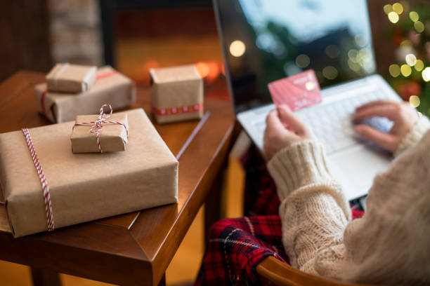 weihnachten. frau in pullover hält kreditkarte mit laptop für die bestellung sitzen am tisch mit verpackung geschenk in der nähe von kamin und weihnachtsbaum. online-shopping-konzept - christmas shopping internet family stock-fotos und bilder