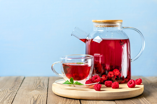 Herbal tea with berries, raspberries, mint leaves and hibiscus flowers in glass teapot and cup on wooden table Medicine for cold Vitamin drink Rustic style.
