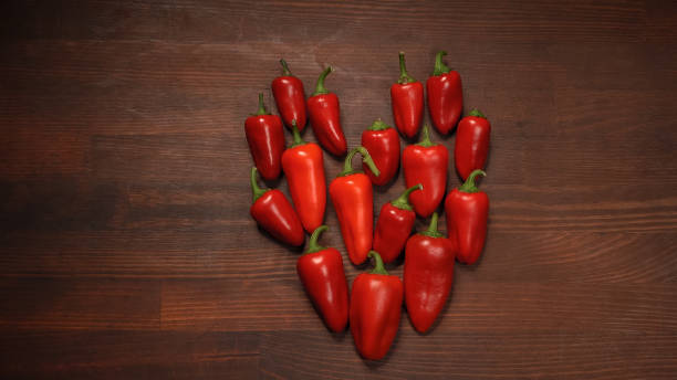 heart shape of chillies or peppers and capsicums or bell peppers. sweet bell, paprika, cayenne, chilli, hungarian wax pepper, isolated on wooden table background - mexico chili pepper bell pepper pepper imagens e fotografias de stock