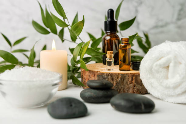 itens de tratamento de beleza para procedimentos de spa em mesa de madeira branca com planta verde. pedras de massagem, óleos essenciais e sal marinho com vela acesa - lastone therapy massaging spa treatment stone - fotografias e filmes do acervo